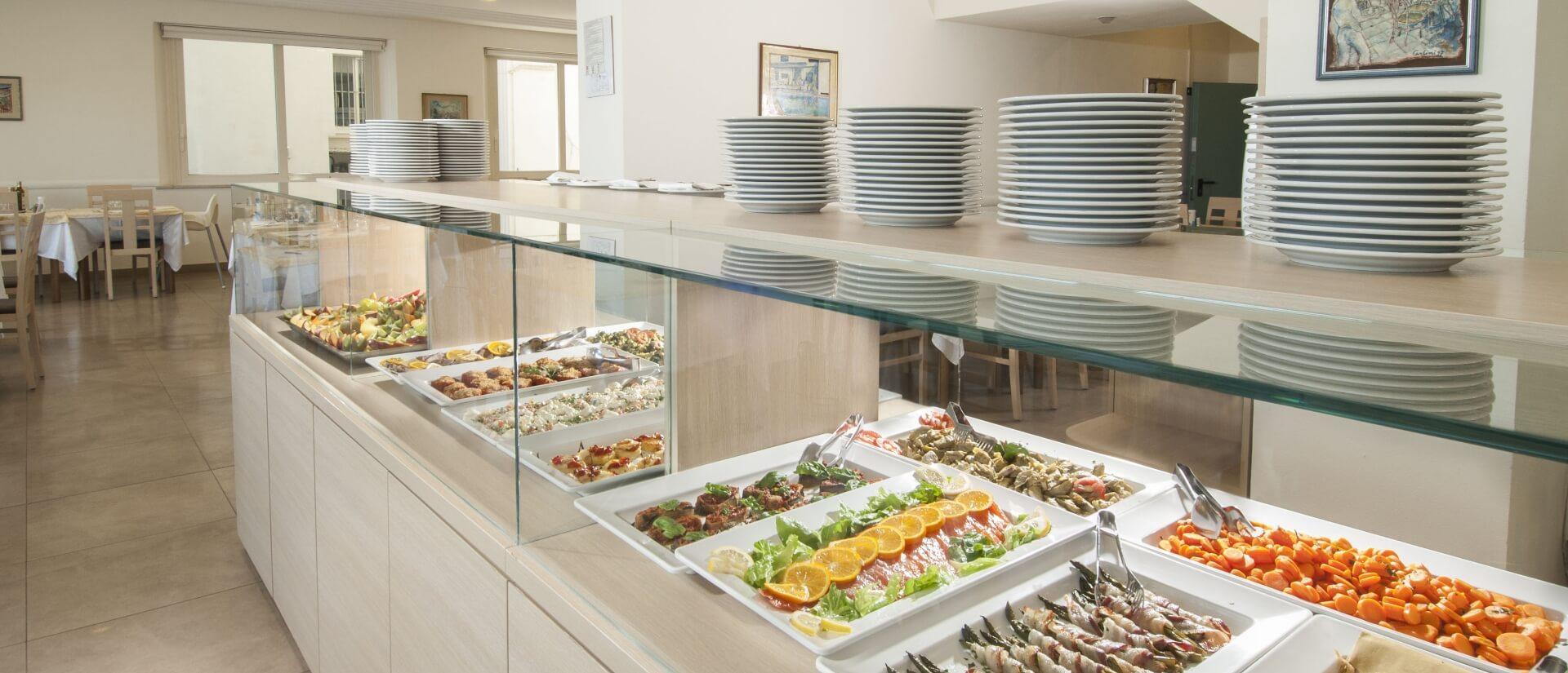 Buffet con piatti assortiti e vassoi di cibo in un ristorante luminoso.
