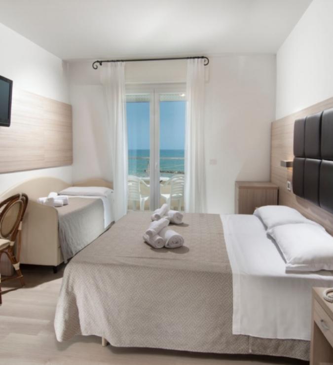 Camera d'hotel con vista mare, letto matrimoniale e arredi moderni.