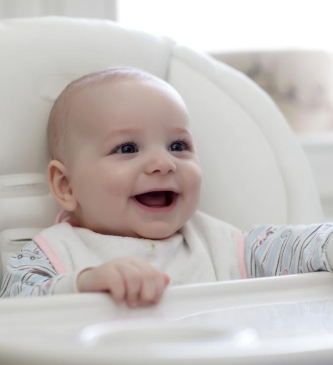 Bambino sorridente seduto su un seggiolone, indossa un bavaglino.
