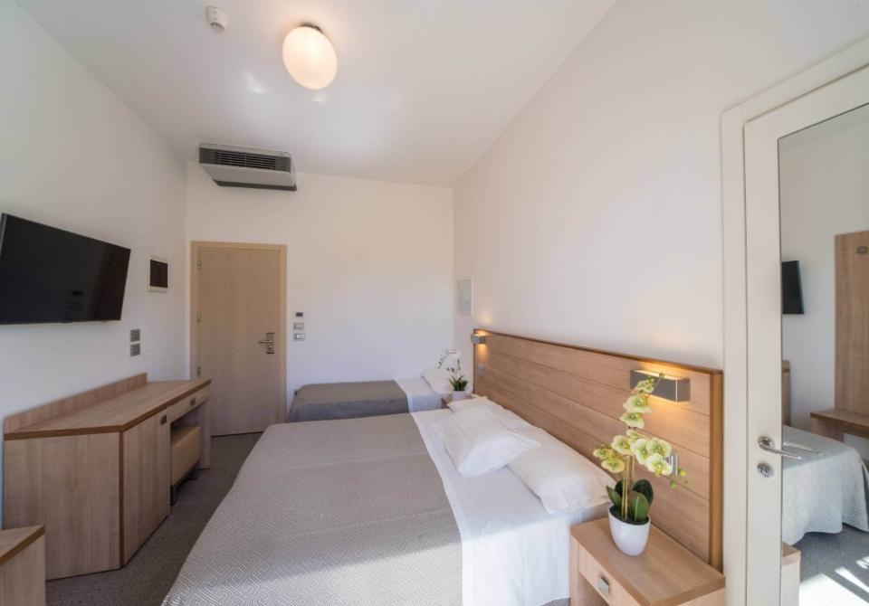 Camera moderna con letto matrimoniale, TV a parete e arredamento in legno chiaro.