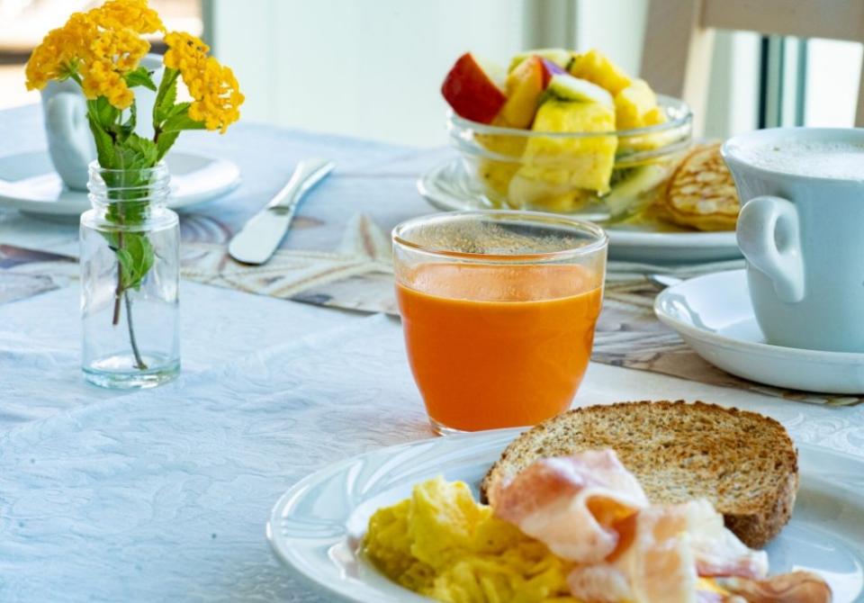 Colazione con uova, pancetta, succo d'arancia, caffè e frutta fresca su tavola apparecchiata.