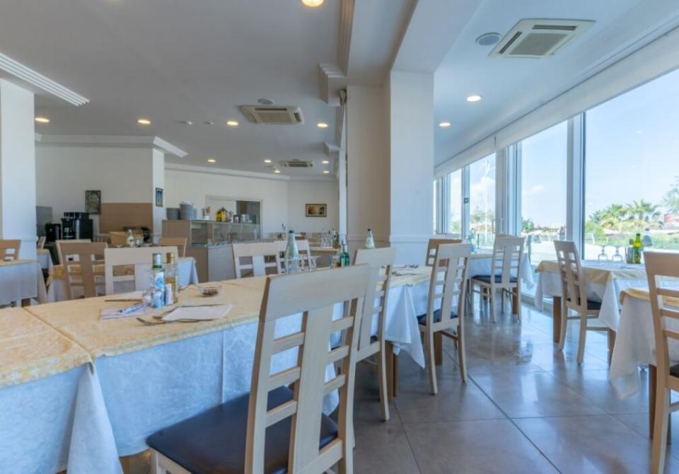 Ristorante luminoso con tavoli apparecchiati, ampie finestre e atmosfera accogliente.
